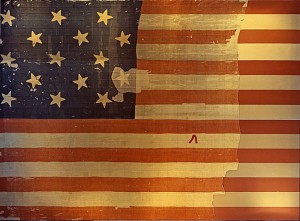 The flag that inspired Francis Scott Key to write what would become “The Star Spangled Banner,” shown on display at the Smithsonian’s National Museum of History and Technology, around 1964. Many pieces were cut off the flag and given away as souvenirs early during its history. A linen backing, attached in 1914, shows the original extent of the flag. Image-Wikipedia