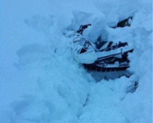 A snowmobile is buried in a snowbank after the operator becomes stranded near Dan Moeller Bowl on Douglas Island near Juneau, Alaska, Jan. 5, 2016. The man was located, hoisted and transported to Juneau by a Coast Guard Air Station Sitka MH-60 Jayhawk helicopter crew. U.S. Coast Guard photo.