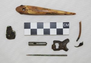 Metal and metal/ivory composite artifacts from Cape Espenberg: a bone fishing lure with iron inset eyes, a piece of bone fishing tackle with a copper hook, an eyed copper needle, a small fragment of sheet copper, a cylindrical bead and buckle fragment. Image credit: H. Kory Cooper et al.