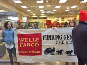 Protesters holding up a banner in front of Wells Fargo's 5th Avenue Mall branch in Anchorage Tuesday. Image-Alaska Rising Tide
