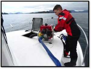 Petty Officer 2nd Class Derrick Depriest, a damage controlman on board the Coast Guard Cutter John McCormick, operates a P-6 pump to combat flooding in the forward living quarters of a tug that ran aground on the Vitskari Rocks, near Sitka. Image-USCG