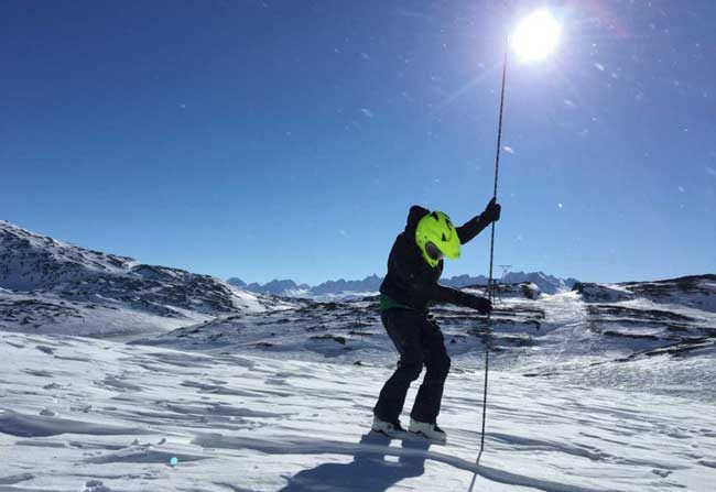 A snowmachiner in Thompson Pass measures snow depth with an avalanche probe. Image-Gabe Wolken