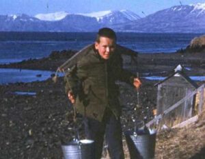 Photo: Boy in Larsen Bay carries water buckets with the help of a wooden yolk. Smith Collection, courtesy of Tim and Norman Smith.
