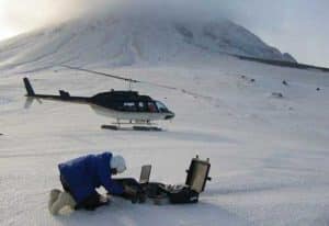 Seismologist John Power, with the U.S. Geological Survey and the Alaska Volcano Observatory, transfers data from the campaign broadband seismometer AU14 on the northeast flank of Mt. Augustine. A debris fan below the northeast chute is visible in the upper right of the image. Photo by Max Kaufman, AVO/UAF GI