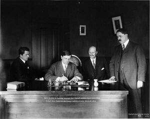 Alfred Shoup, Conrad Freeding, W.W. Shorthill watch Governor Walter E. Clark sign the sufferage bill. Image-Public Domain