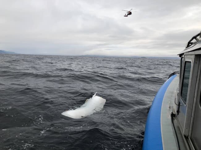 Alaska Wildlife troopers pull up to debris thought to be from the ill-fated Guardian Flight aircraft as a Coast Guard MH-60 hovers overhead. Image-AWT