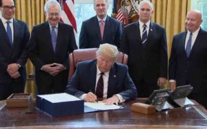 Trump signing $2 trillion Coronavirus Relief bill as Republicans and others look on. 