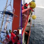 {left)Scientists prepare to deploy ocean moorings used to understand sea ice loss in the eastern Arctic Ocean.(right)Large yellow floats connected to several scientific sensors are lowered over the edge of a ship in the Arctic Ocean. Photos courtesy of the Nansen and Amundsen Basins Observational System
