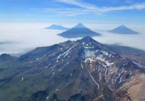An aerial oblique photo of the volcanoes in the Islands of Four Mountains, Alaska, taken in July 2014. In the center is the summit of Mount Tana. Behind Tana are (left to right) Herbert, Cleveland, and Carlisle volcanoes. Image credit: John Lyons / USGS.