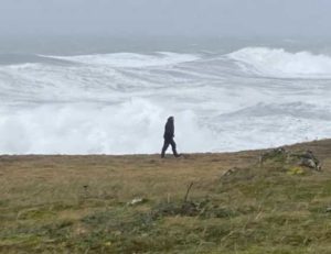 Filmmaker Fritz Mueller walks at the edge of St. Paul Island as waves crash ashore, driven by the remnants of Typhoon Merbok as it passes over St Paul Island. Photo by Chris Maio