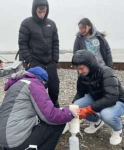 Gay Sheffield (bottom left) at the Port of Nome with Nome-Beltz High School science students filtering seawater to detect and identify the types of algae in the area — on an unusually rainy mid-November day.
