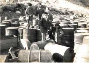 Photo: Children playing on empty fuel barrels, Armstrong Collection.
