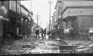 UAF archive photo. This photograph shows Front Street in Nome, Alaska, during a storm on Oct. 7, 1913. Anvil Bakery, Anvil Coffee Shop, Merchants Cafe and S.L. Lewis clothing store are visible.