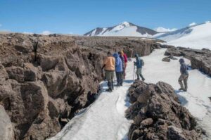 Photo by Seth Adams
Students examine cracks formed after lava that flowed over the Mageik Glacier in Alaska’s Katmai National Park and Preserve. Lava flowed over the ice, then left a hanging shelf of rock after the glacier melted from under it. The shelf collapsed, leaving cracks where it split from the rest of the flow.